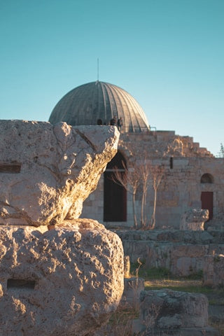 Stone ruins with a domed building in the background under a clear blue sky.