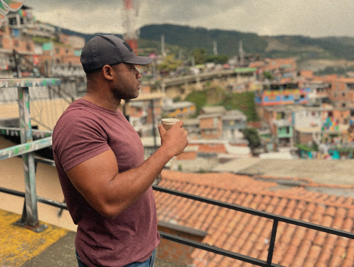 Man in a maroon shirt standing and holding a cup while overlooking a colorful cityscape.