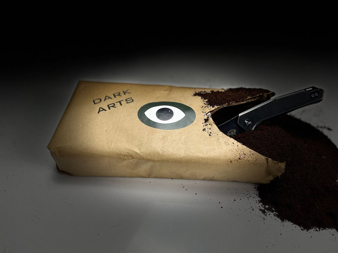 Opened bag of 'DARK ARTS' coffee with ground coffee spilling out and a black knife resting on the pile.