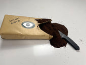 Opened 'DARK ARTS' coffee bag with ground coffee spilling out and a black knife resting beside it on a white surface.